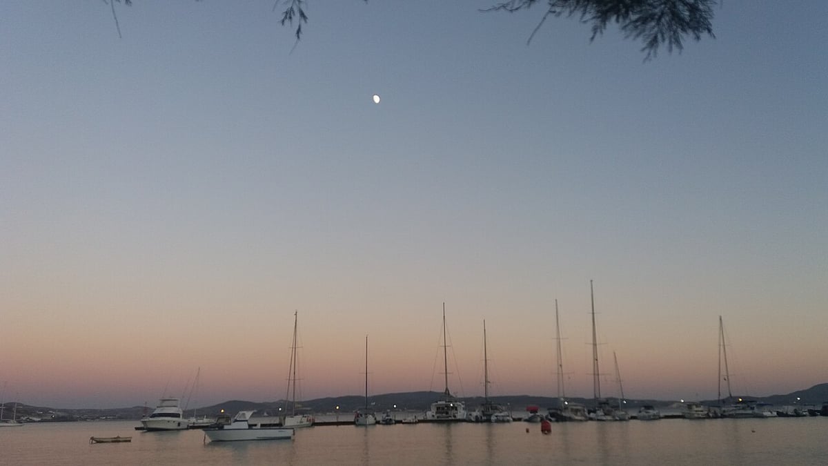 Δρομολόγια πλοίων Μήλος: ο κόλπος του Αδάμαντα στο σούρουπο, με ιστιοφόρα δεμένα στο λιμάνι