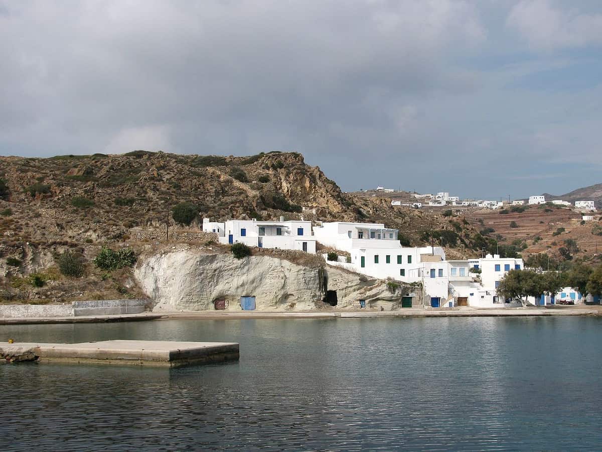 Εκδρομή Κίμωλος: το λιμάνι της Ψάθης με λευκά σπίτια πάνω από την προκυμαία και ήρεμη θάλασσα