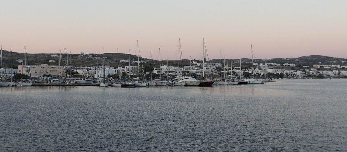 Adamantas: sailing yachts moored along the harbour of the port of Milos at dusk, with the white houses of the town behind