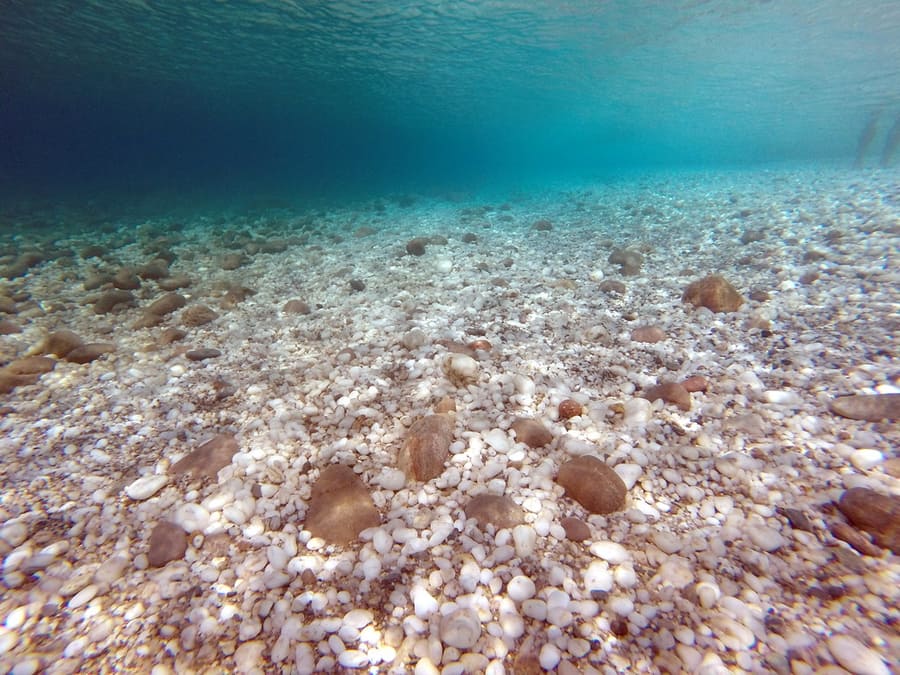 Agia Kyriaki beach: clear turquoise water over white and brown pebbles, seen from under the surface
