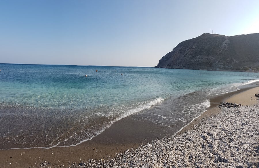 Agia Kyriaki beach: small waves on a long shore of sand and pebbles, with a dark headland at the end of the bay