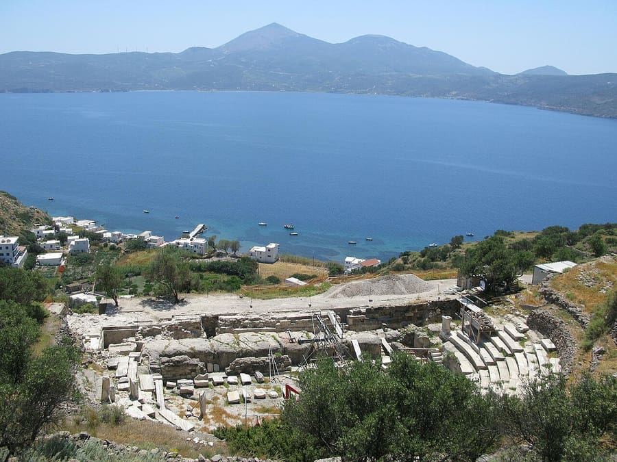 Ancient theatre of Milos: the marble rows of seats on the hillside above the blue bay, with houses by the shore below
