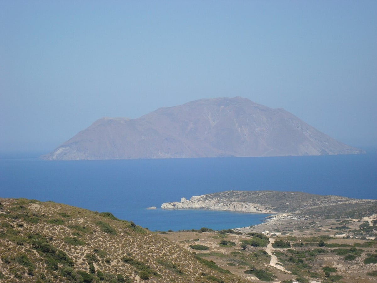 Antimilos: the bare volcanic islet rising from a deep blue sea, seen across the water from the hills of Milos