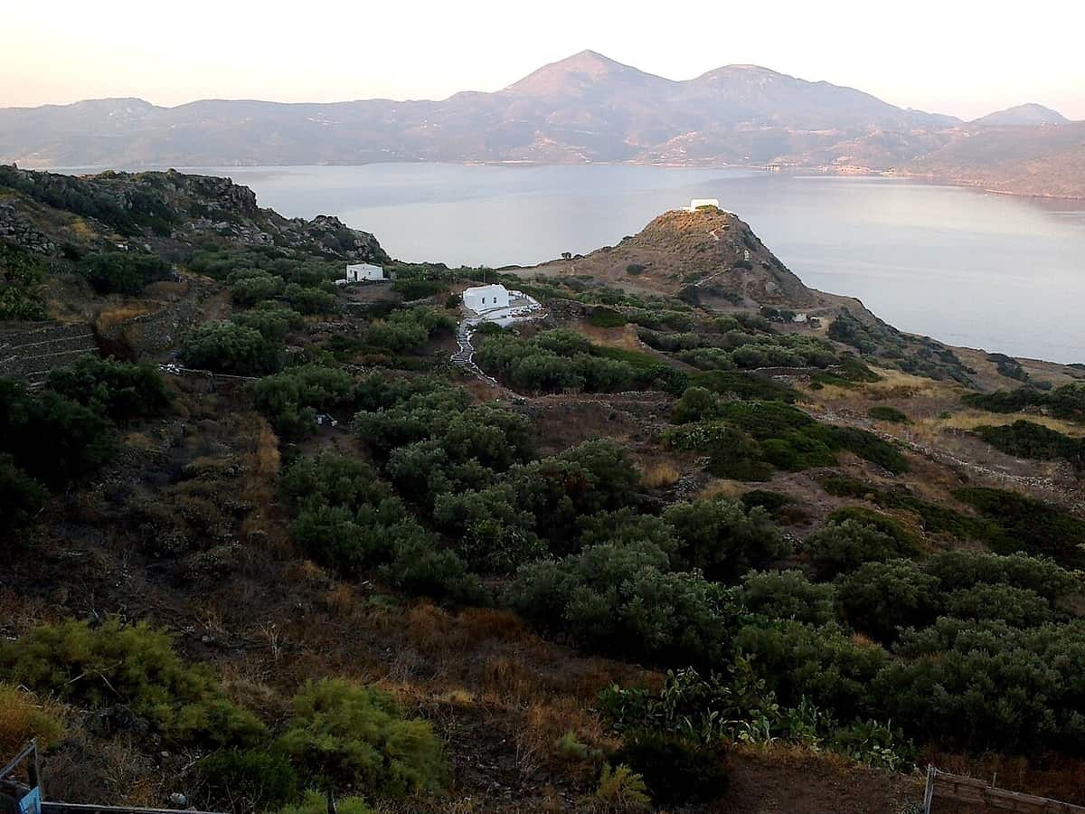 Apartments in Milos: view from the hillside below Plaka over a white chapel on a hill and the bay of Milos