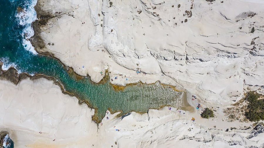 Best time to visit Milos: swimmers in the narrow turquoise inlet of Sarakiniko between smooth white rocks