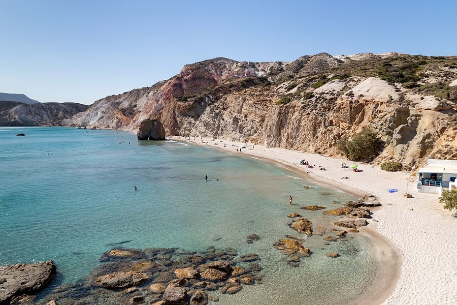 Milos boat rental: Firiplaka beach from above, with clear shallow water, rocks and tall colourful cliffs