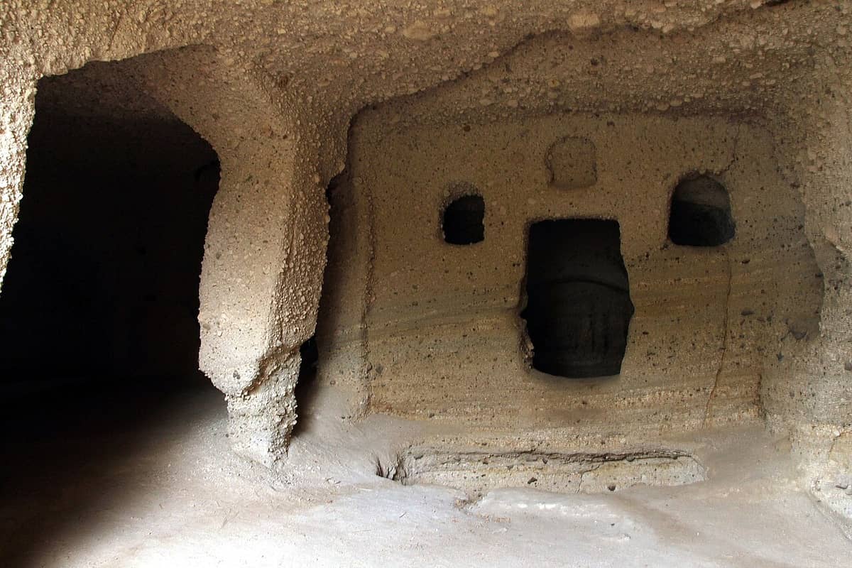 Catacombs of Milos: an arched tomb chamber cut into the soft volcanic rock, with burial niches in the wall beside a dark corridor