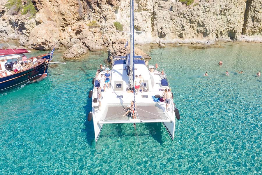 Milos catamaran cruise: people swimming around an anchored catamaran in clear shallow water below the cliffs of Kleftiko