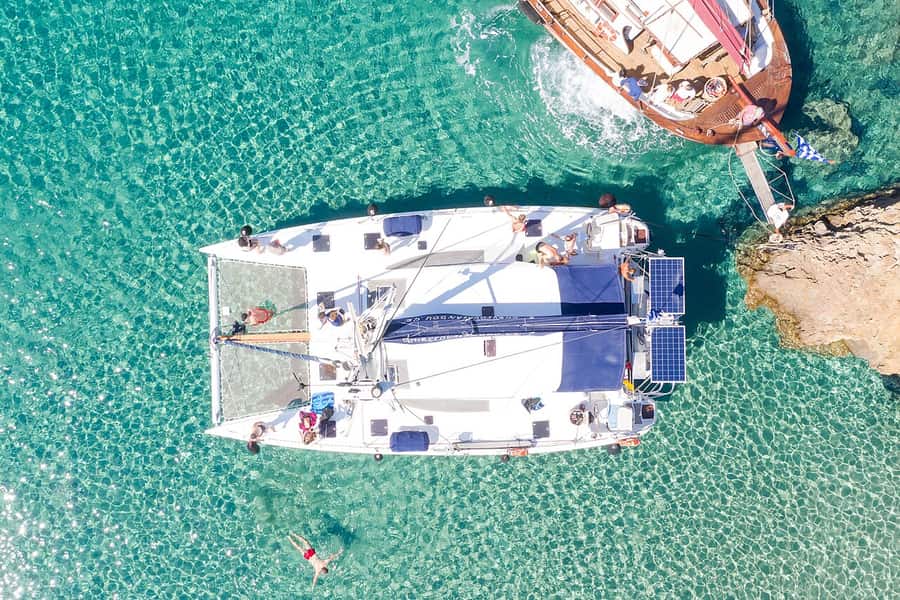Milos catamaran cruise: a catamaran seen from above at Kleftiko, with its two hulls, the deck nets and swimmers in the turquoise water