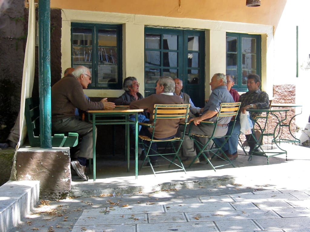 Coffee and drinks in Zefiria: village men sitting around tables outside a traditional Greek kafeneio on a paved terrace