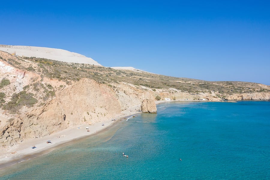 Firiplaka beach: the long curve of sand below pale volcanic cliffs, with turquoise water and a rock pillar near the shore