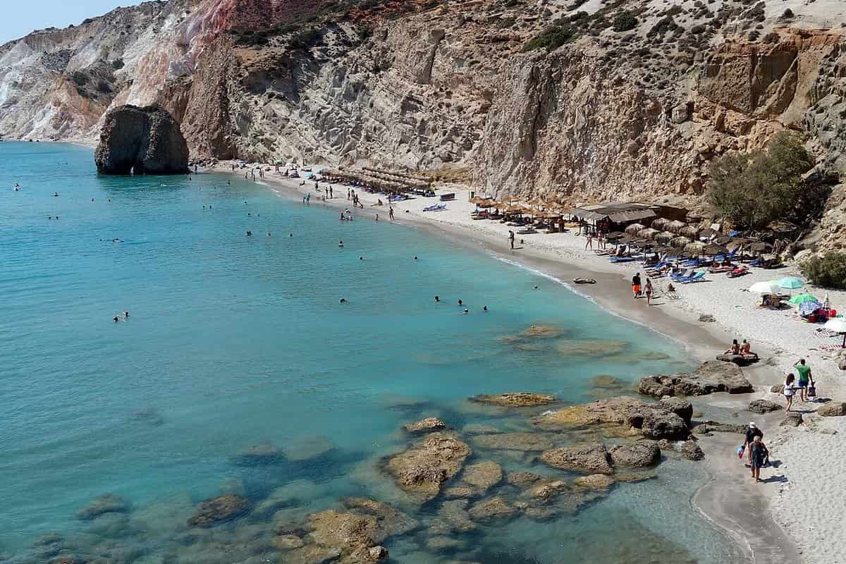 Firiplaka beach: the rock pillar in shallow turquoise water in front of coloured volcanic cliffs