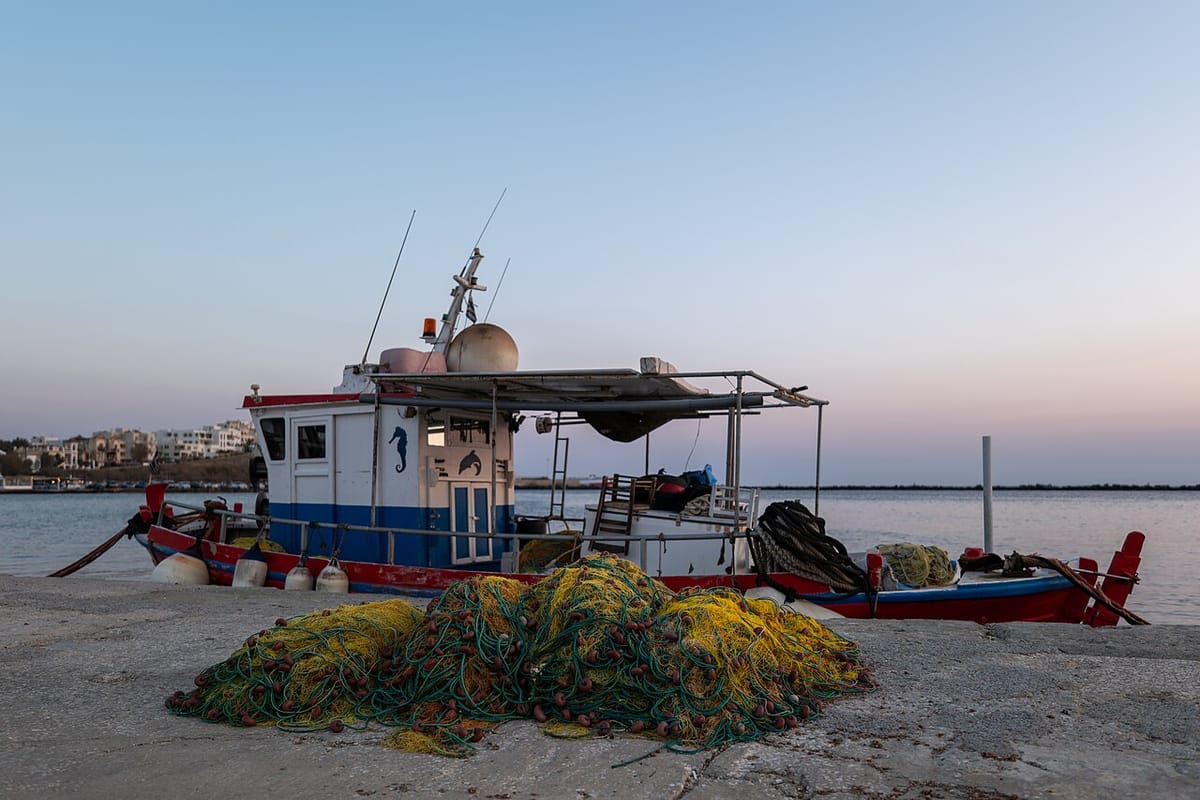 Milos fishing trip: a small Greek fishing boat on the quay with a pile of yellow and green nets in the evening light