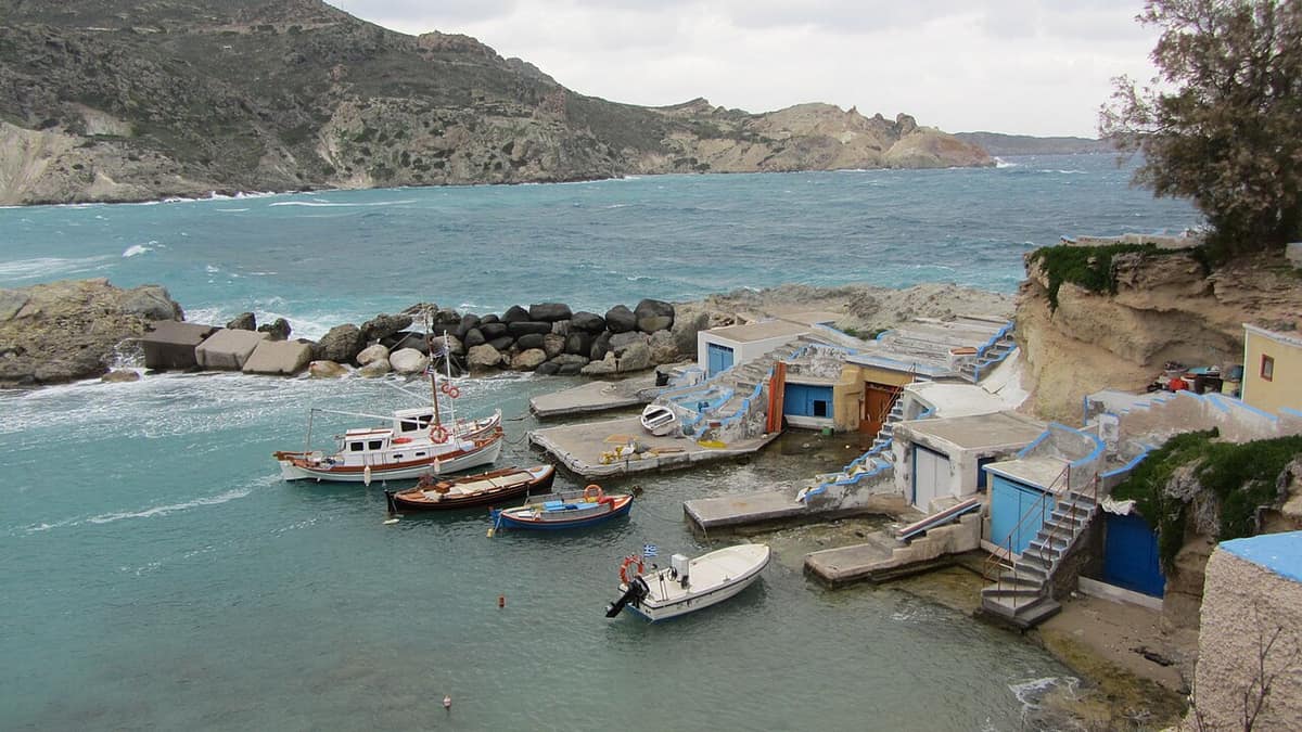 Milos fishing trip: small fishing boats moored in the cove of Mandrakia, below the painted doors of the boathouses