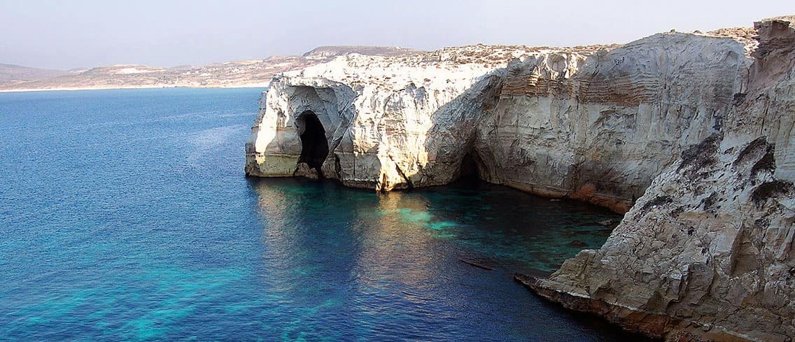 White rock cliffs and a sea cave above turquoise water on the coast of Milos