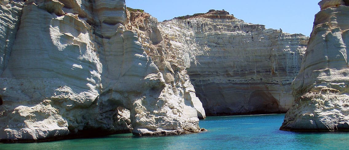 Tall white cliffs around a channel of green water on the coast of Milos