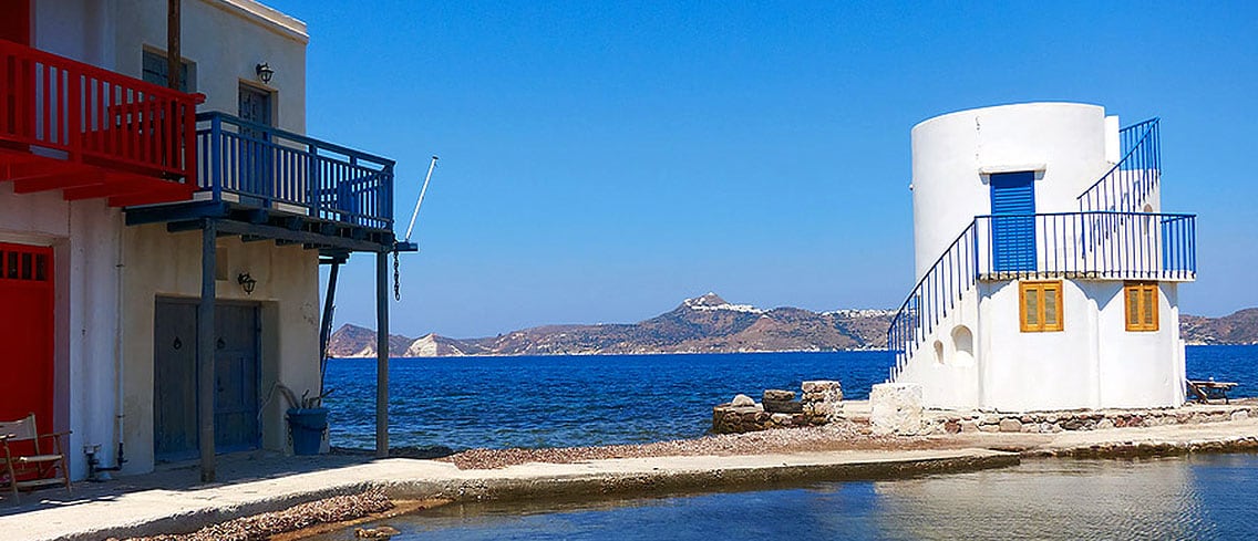 Painted boathouse balconies and a small white tower by the sea in Milos