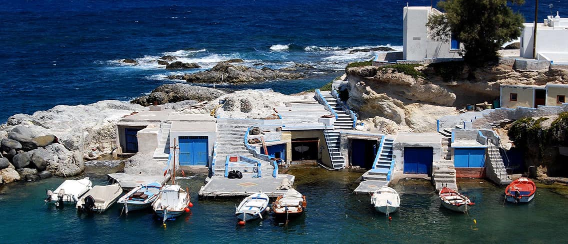 Small boats moored in front of the boathouses of a fishing cove in Milos