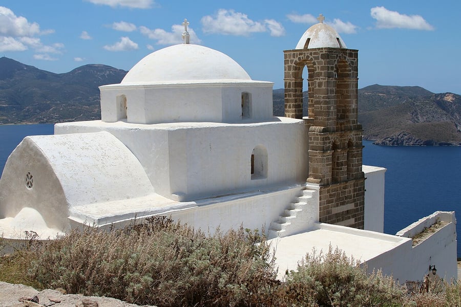 Milos honeymoon: the white church of Panagia Thalassitra and its stone bell tower on the castle hill above Plaka, with the bay behind