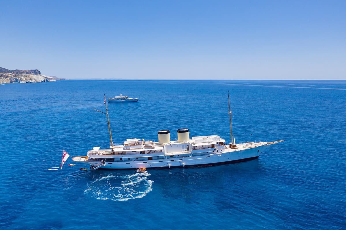 Milos honeymoon: a large two-masted yacht at anchor in the deep blue water off Kleftiko, with a small boat beside it