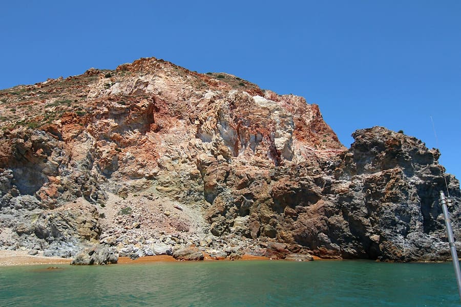Milos hot springs: red, yellow and grey volcanic cliffs above green water in the bay of Thiafes, near the old sulphur mines