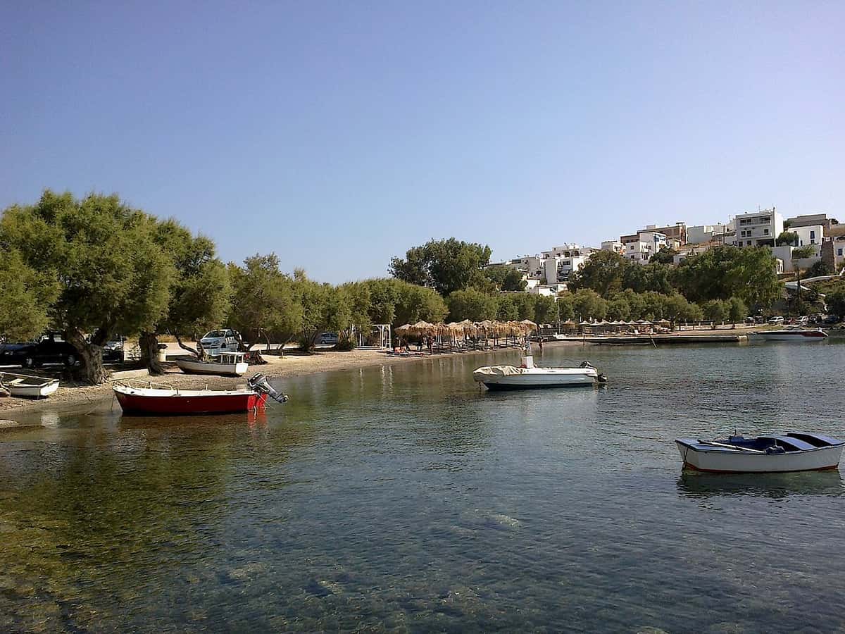 Hotels in Milos: white buildings above the tree-lined beach of Lagada in Adamantas, with small boats in the bay