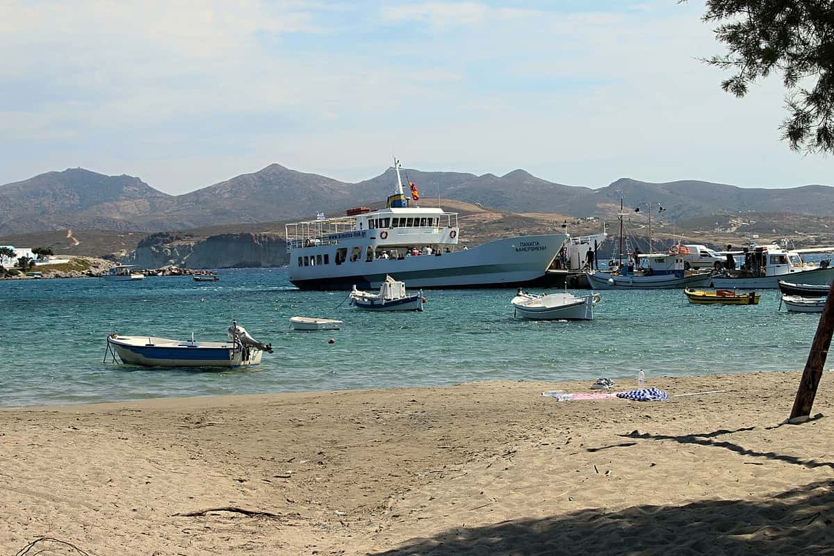 How to go to Milos: the small ferry to Kimolos moored at the harbour of Pollonia, with fishing boats and the sandy beach in front