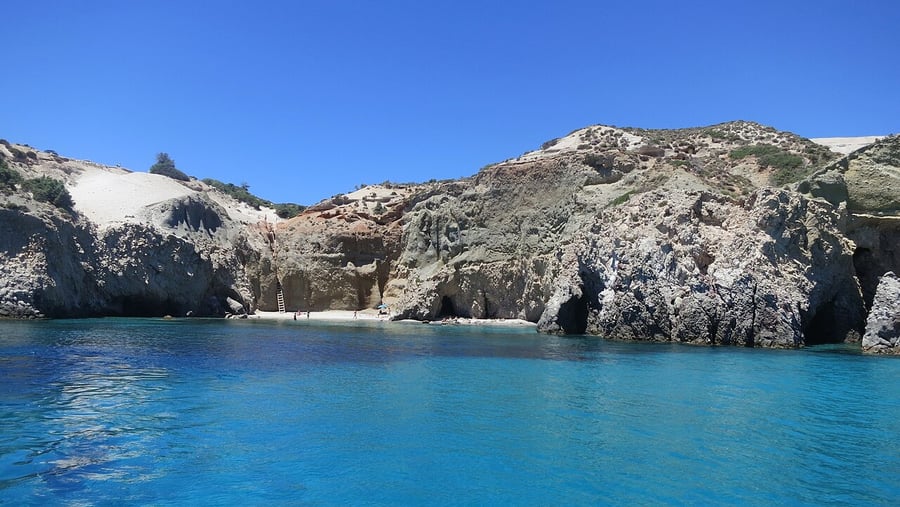Is Milos expensive: a small beach below white and grey cliffs with clear blue water on the south coast of Milos