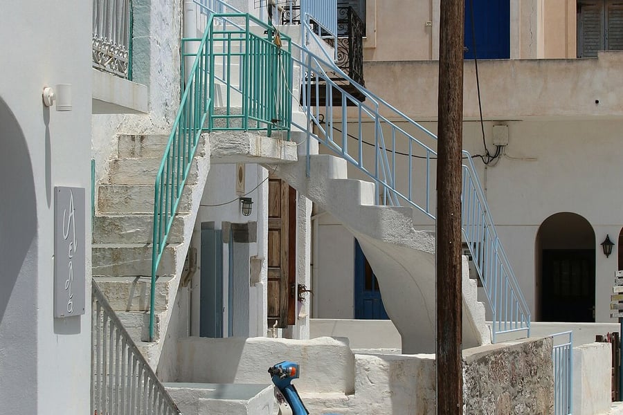 Is Milos expensive: white houses, blue rails and outdoor stairs on a lane in Plaka, a village that is free to walk
