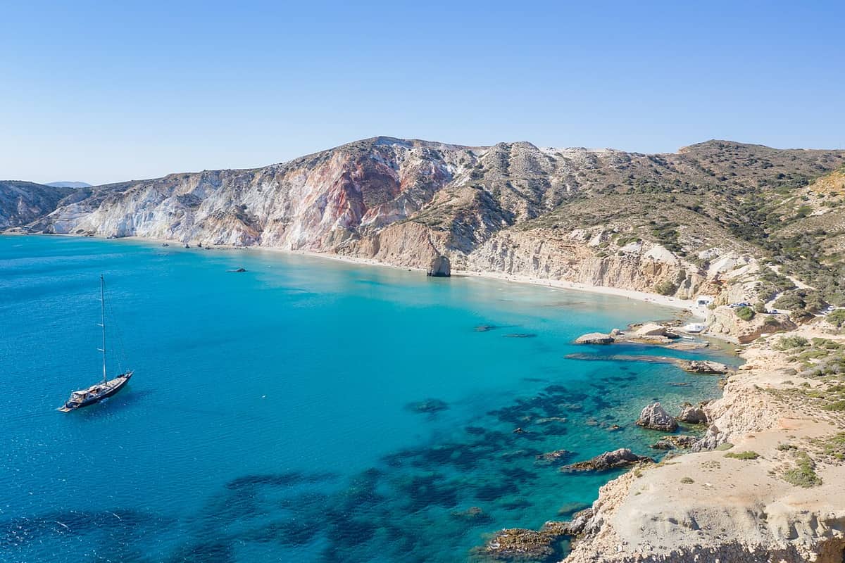 Milos jeep tour: bare hills, coloured cliffs and a turquoise bay on the wild south coast of Milos, seen from above
