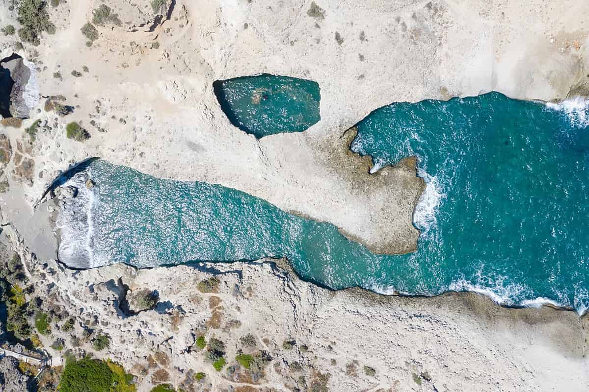 Kayak and hike Milos: turquoise sea inlets cut into white volcanic rock on the north coast of Milos, seen from above