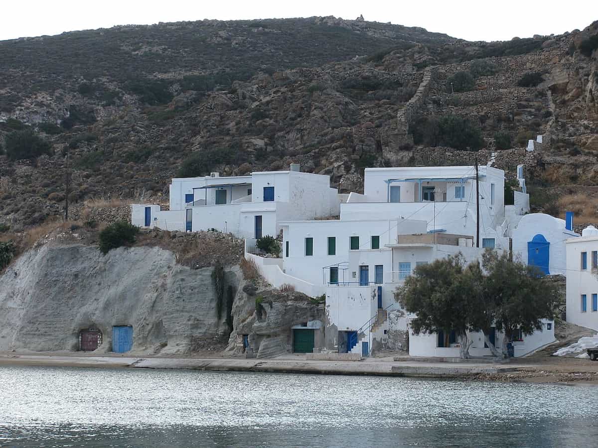 Kayak Kimolos: white houses with blue doors along the waterfront of Psathi, the harbour of Kimolos, below a dry hillside