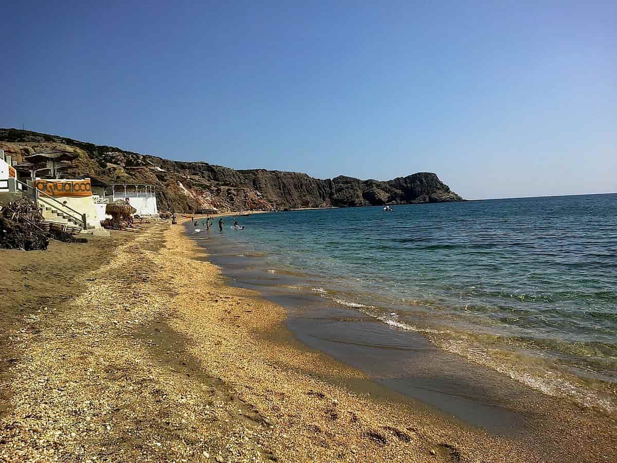 Kayak Paleochori: the long beach of Paleochori with dark golden sand below layered red and ochre cliffs on the south-east coast of Milos