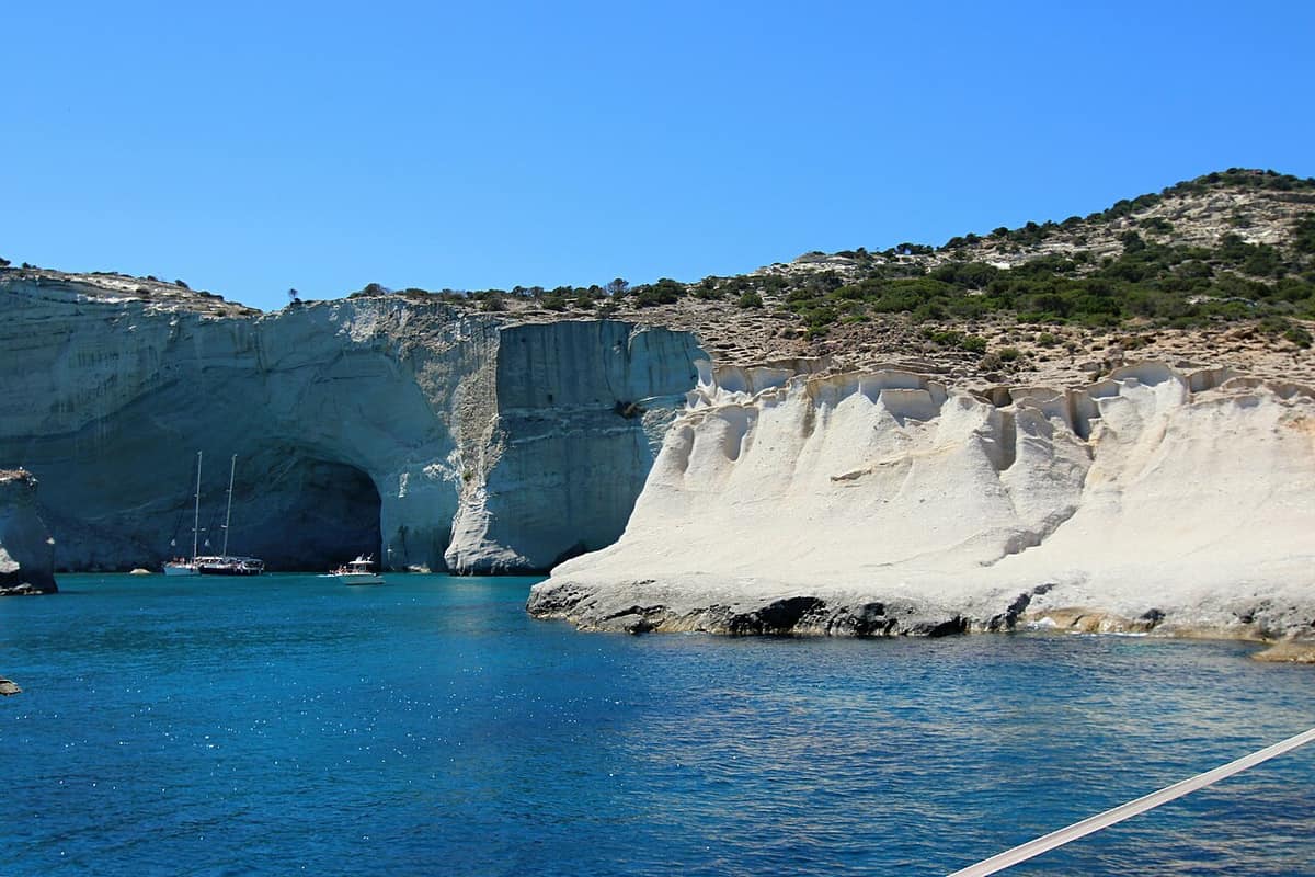 Kleftiko boat tour: the white cliffs and sea caves of Kleftiko seen from a boat, with sailing yachts anchored in the blue water