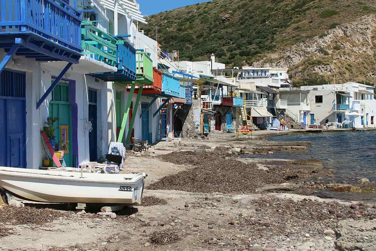 Klima: boathouses with painted doors and balconies along the shore, with a boat pulled up on the beach