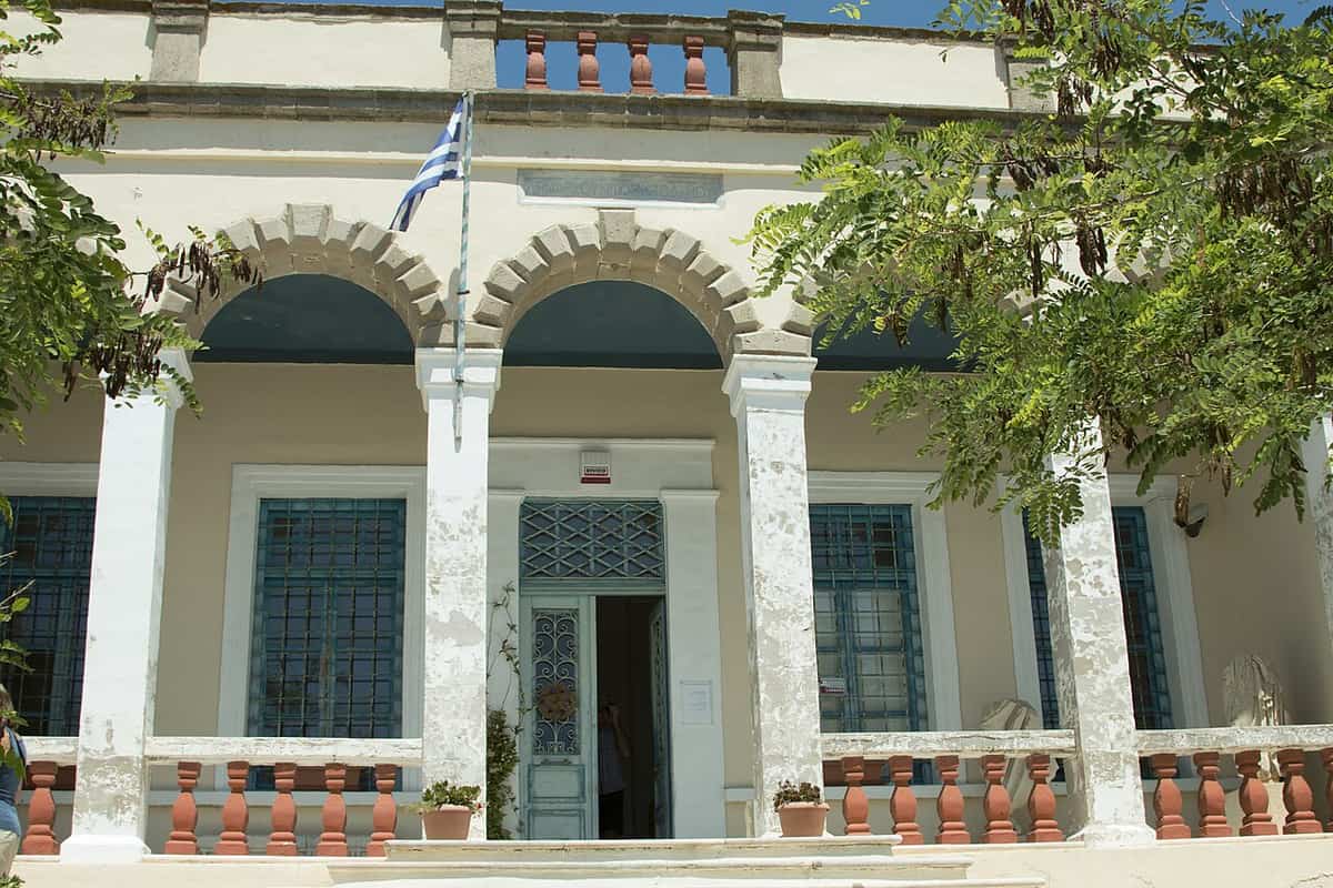 Museums of Milos: the arched front porch of the Archaeological Museum in Plaka, with a Greek flag above the door