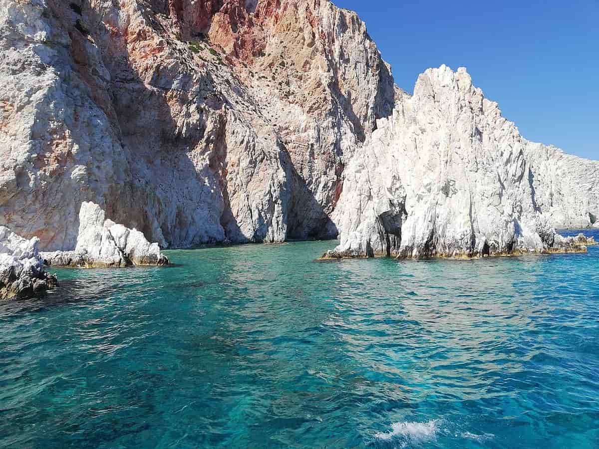 One day cruises from Pollonia: white and red rock pinnacles above clear turquoise water on the coast of Polyaigos