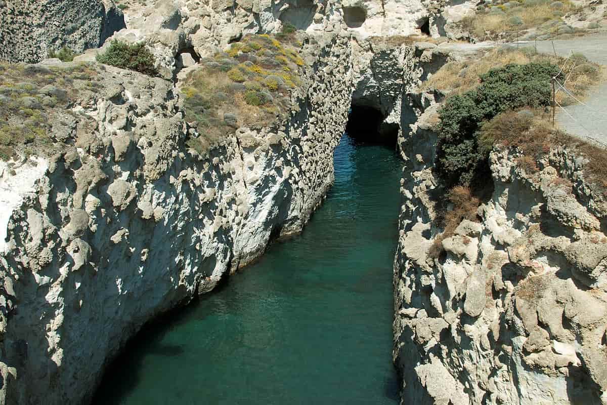 Papafragas hike Milos: the narrow sea gorge of Papafragas between pale volcanic cliffs, with green water running to a rock arch