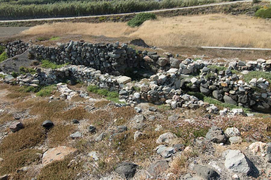 Phylakopi: low stone walls of the sanctuary area and the defensive wall among dry grass at the Bronze Age site