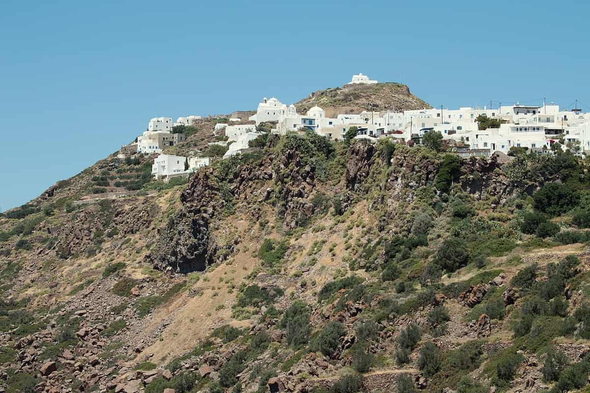 Plaka hike Milos: the white houses of Plaka along the ridge above a steep rocky slope, seen from the path at Tramythia