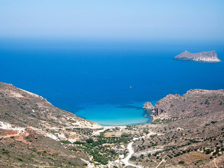 Plathiena beach: the turquoise bay and sandy cove on the north-west coast of Milos seen from the hills above, with an islet offshore