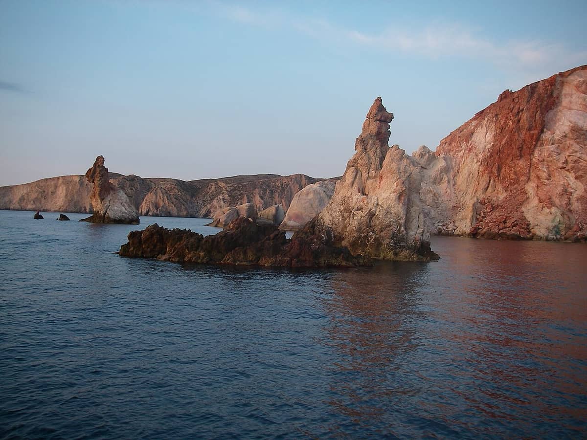 Plathiena kayak Milos: the Arkoudes rock pillars rising from calm water below red and white cliffs on the north-west coast of Milos