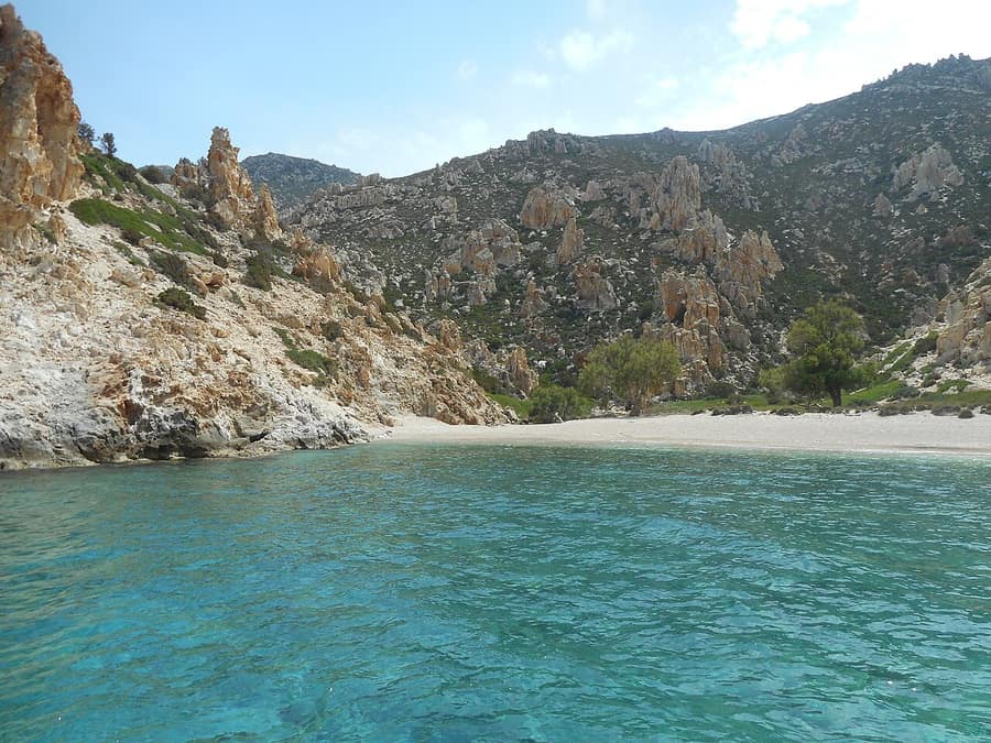 Polyaigos boat trip: a quiet sandy beach with clear green water and tall rock spires on the hills of Polyaigos