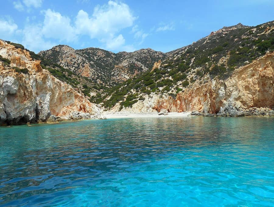 Polyaigos boat trip: a turquoise bay below red, yellow and grey cliffs on the uninhabited island of Polyaigos