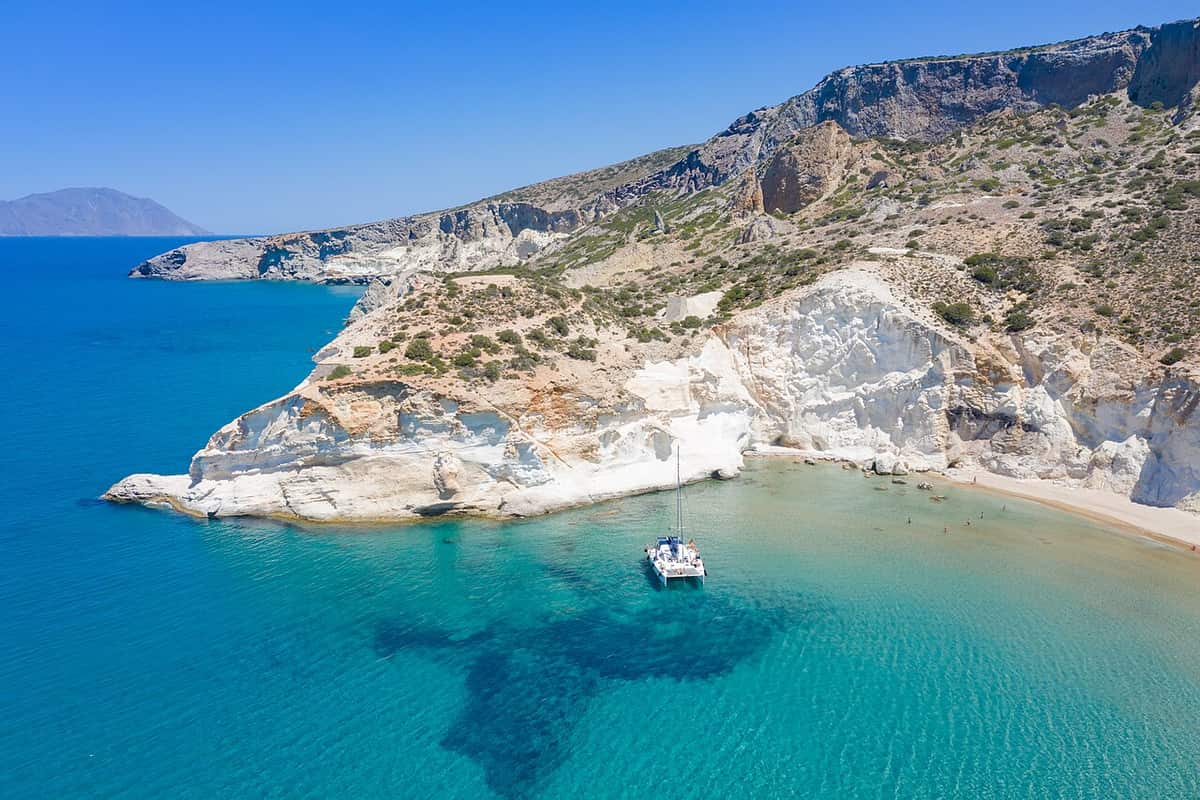 Milos private boat tour: a lone small boat at anchor below white cliffs and a quiet beach on the south-west coast near Kleftiko