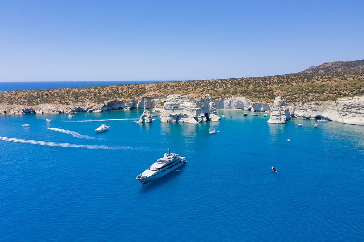 Milos private boat tour: a white motor yacht in the deep blue bay of Kleftiko, with smaller boats near the white rocks
