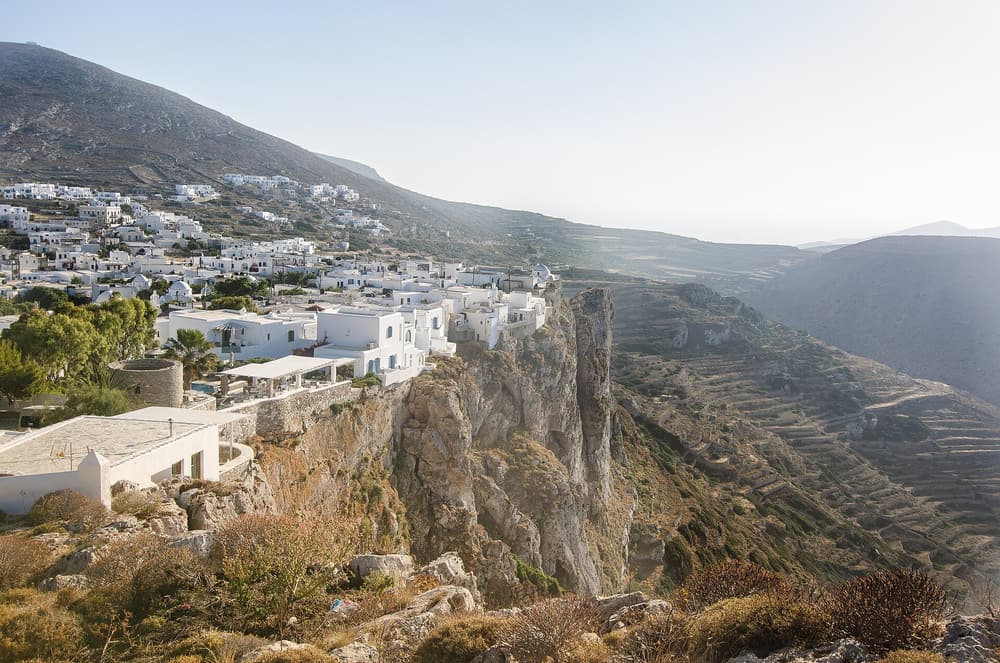 Rent a car Folegandros: the white houses of Chora on the edge of a high cliff above the sea, with terraced hills behind