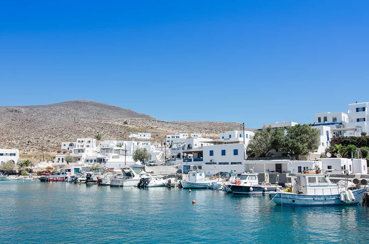 Rent a car Folegandros: the port of Karavostasis with small boats in clear blue water and white houses on the shore