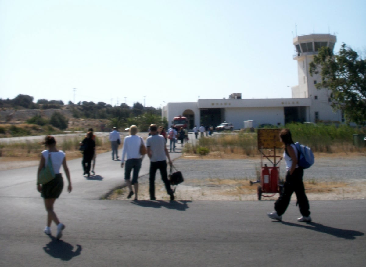 Rent a car Milos: travellers walking from the plane to the small terminal and control tower of Milos airport