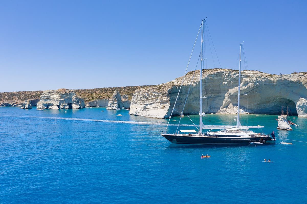 Milos sailing tour: a two-masted sailing yacht in deep blue water in front of the white rocks and sea caves of Kleftiko